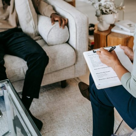 From above crop African American male in casual clothes sitting on comfy couch and answering professional female consultant questions in modern psychotherapy office
